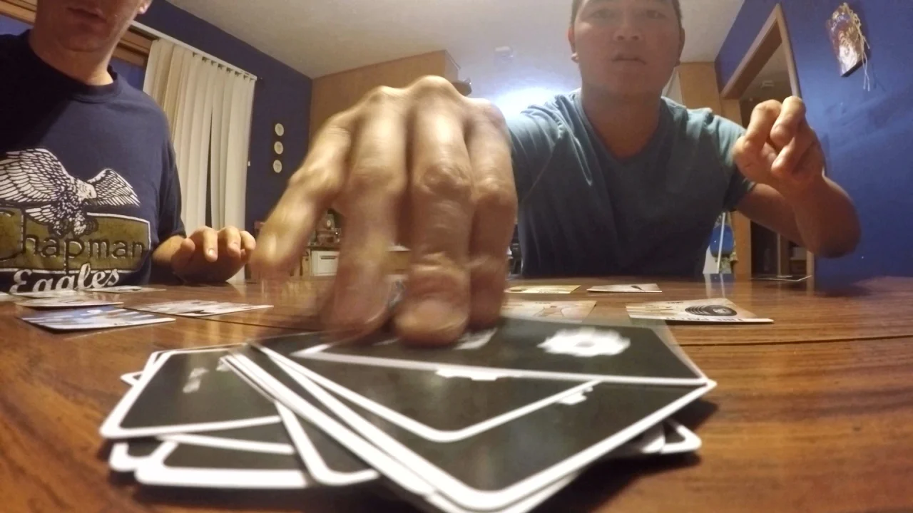 Two players mid-game — one slamming a hand down on the pile of cards on the table.